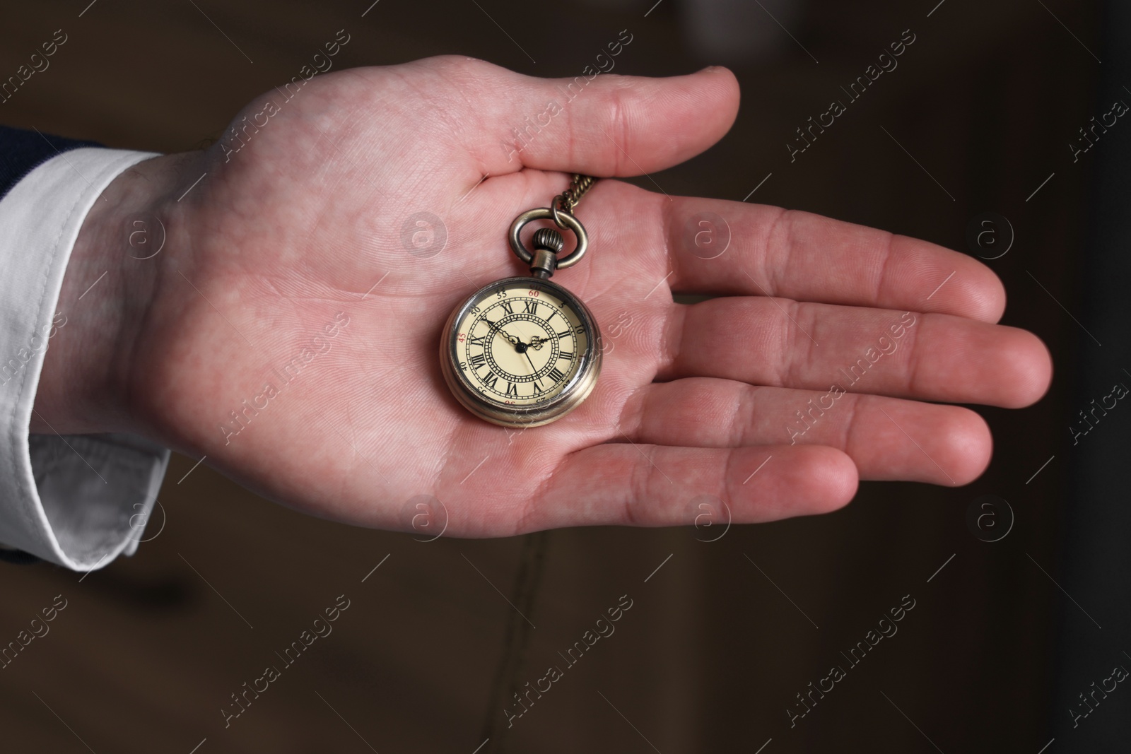 Photo of Man holding chain with elegant pocket watch on blurred background, closeup