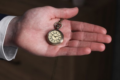 Man holding chain with elegant pocket watch on blurred background, closeup