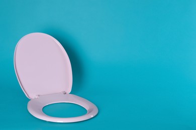 New pink plastic toilet seat on light blue background, space for text