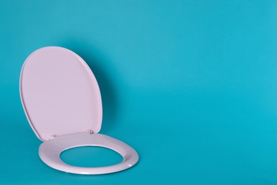 Photo of New pink plastic toilet seat on light blue background, space for text