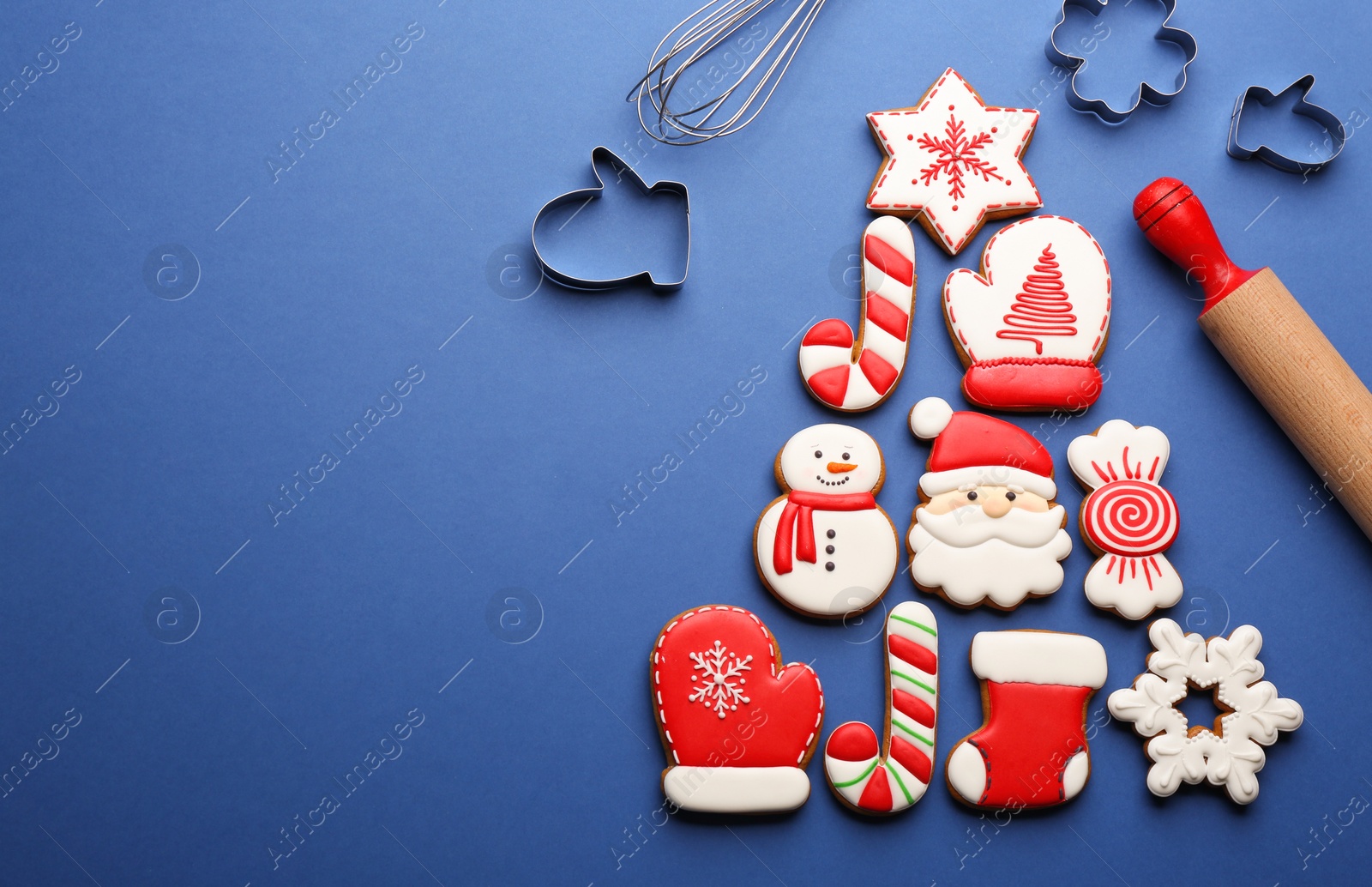 Photo of Kitchen utensils near Christmas tree shape made of delicious gingerbread cookies on blue background, flat lay. Space for text