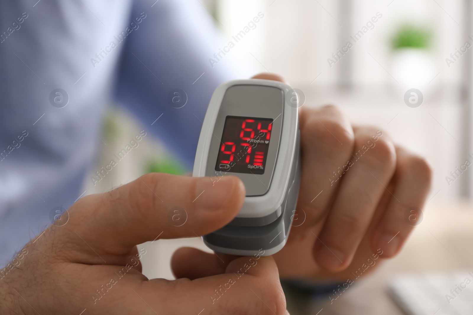 Photo of Man measuring oxygen level with modern fingertip pulse oximeter at workplace, closeup