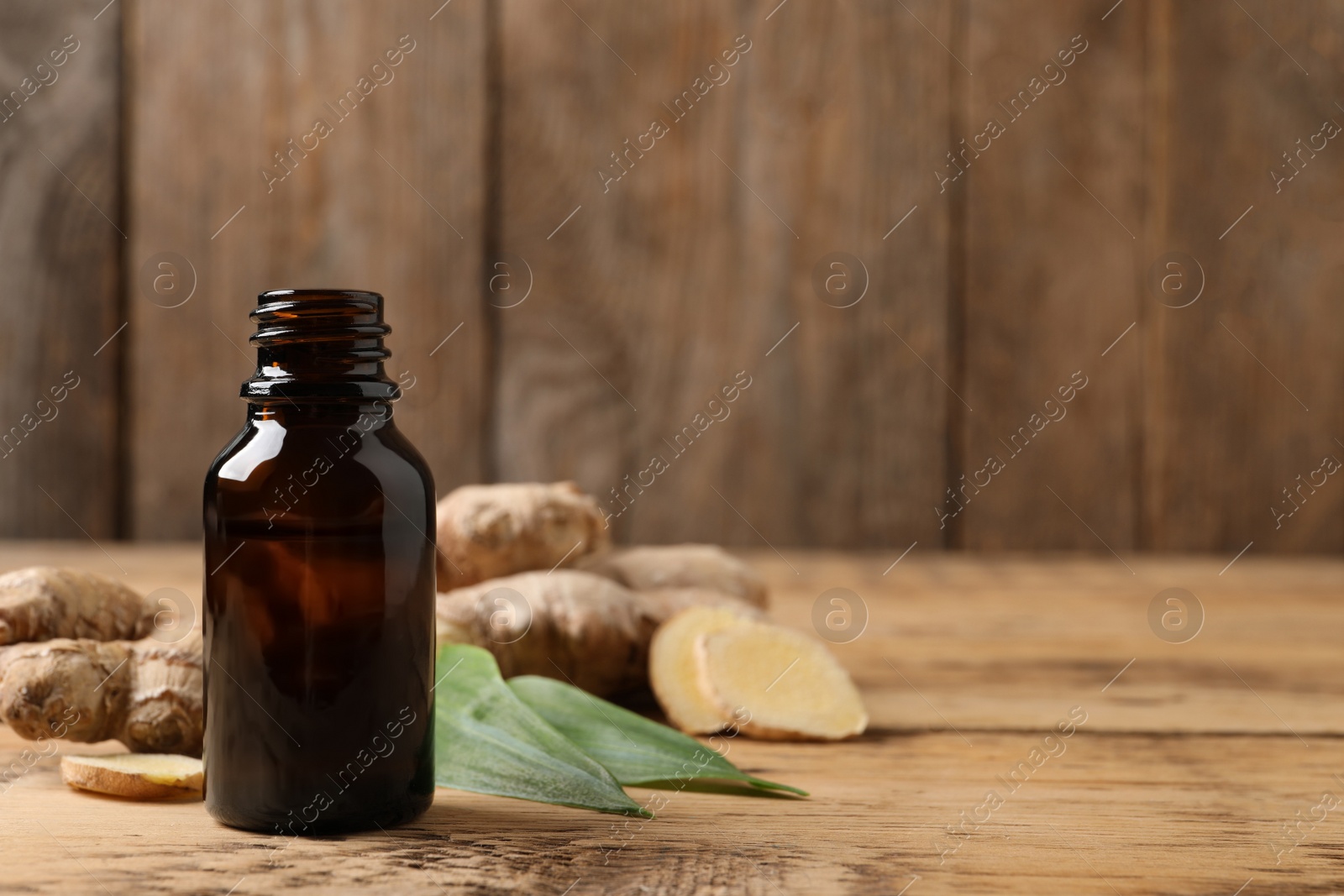 Photo of Glass bottle of essential oil and ginger root on wooden table, space for text