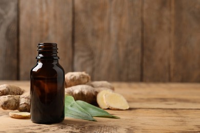 Glass bottle of essential oil and ginger root on wooden table, space for text