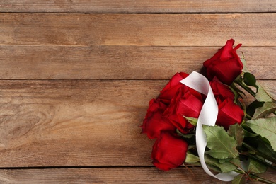 Beautiful red roses with white ribbon and space for text on wooden background, top view. Valentine's Day celebration