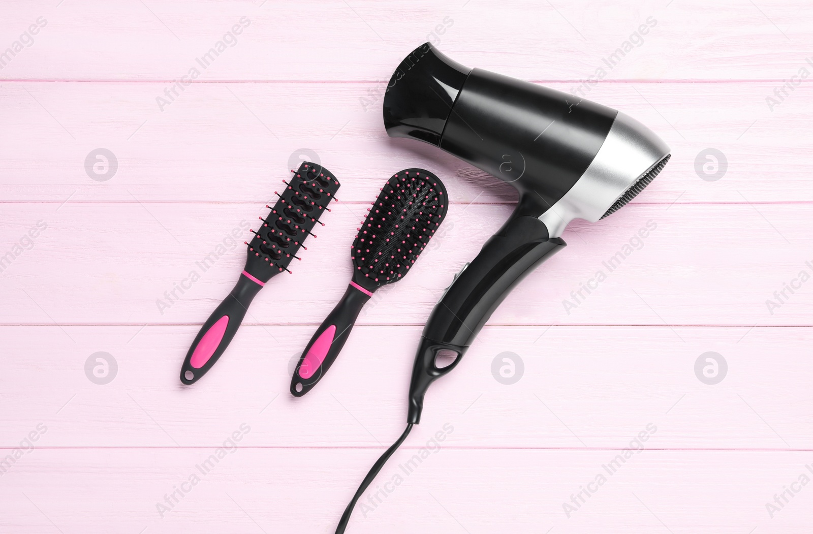 Photo of Hair dryer and brushes on pink wooden table, flat lay. Professional hairdresser tool