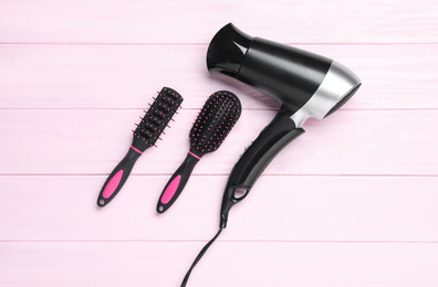 Hair dryer and brushes on pink wooden table, flat lay. Professional hairdresser tool