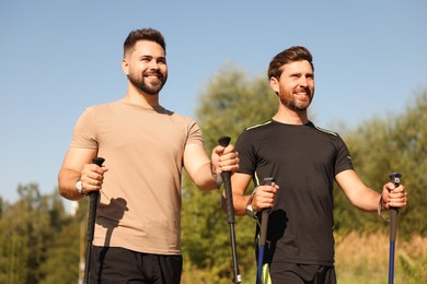 Photo of Happy men practicing Nordic walking with poles outdoors on sunny day