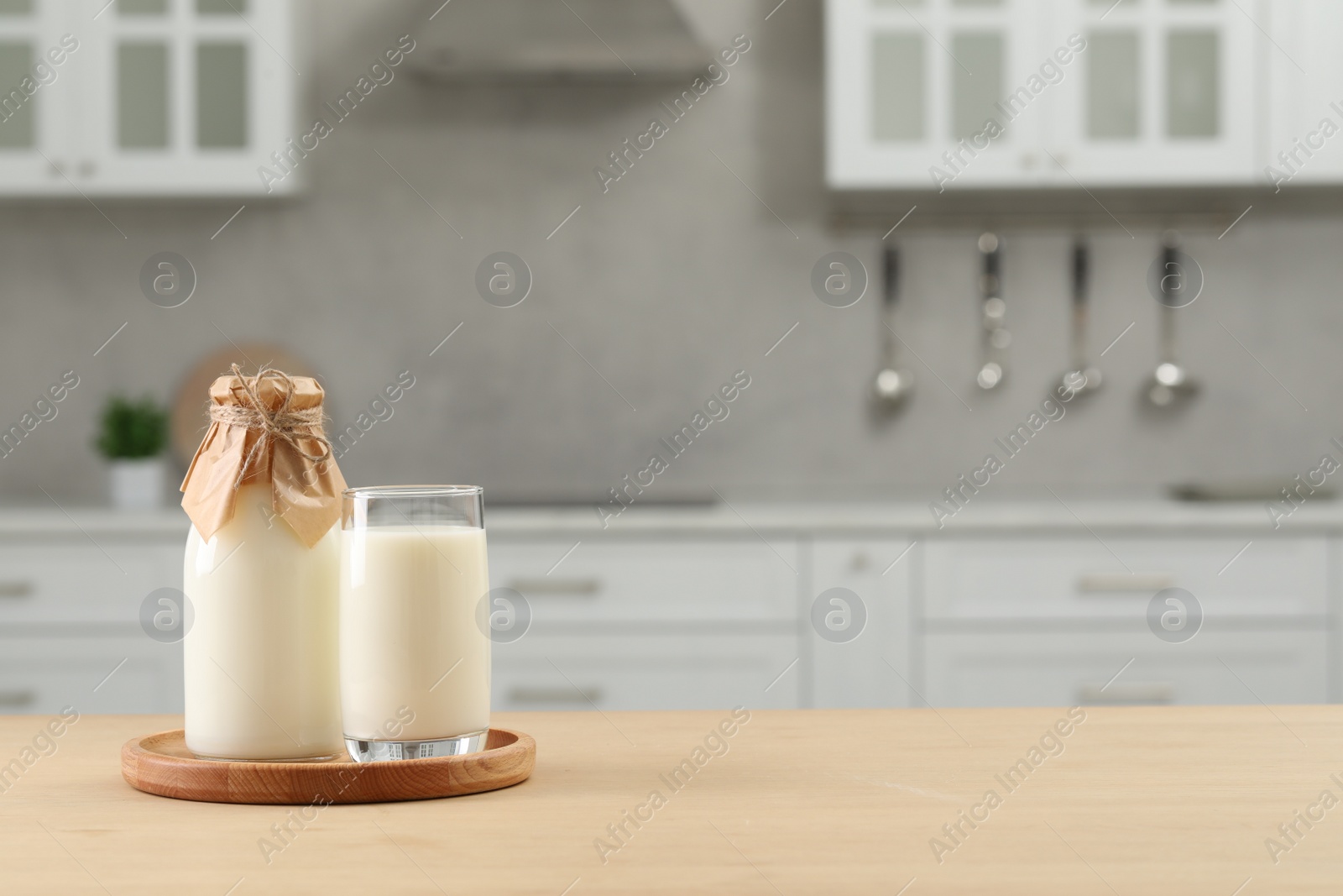 Photo of Bottle and glass with milk on wooden table in kitchen, space for text