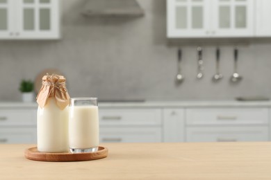Photo of Bottle and glass with milk on wooden table in kitchen, space for text