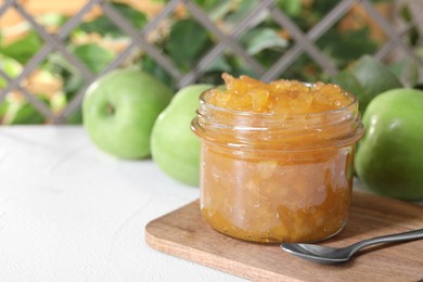 Photo of Glass jar of delicious apple jam and fresh fruits on white table, space for text