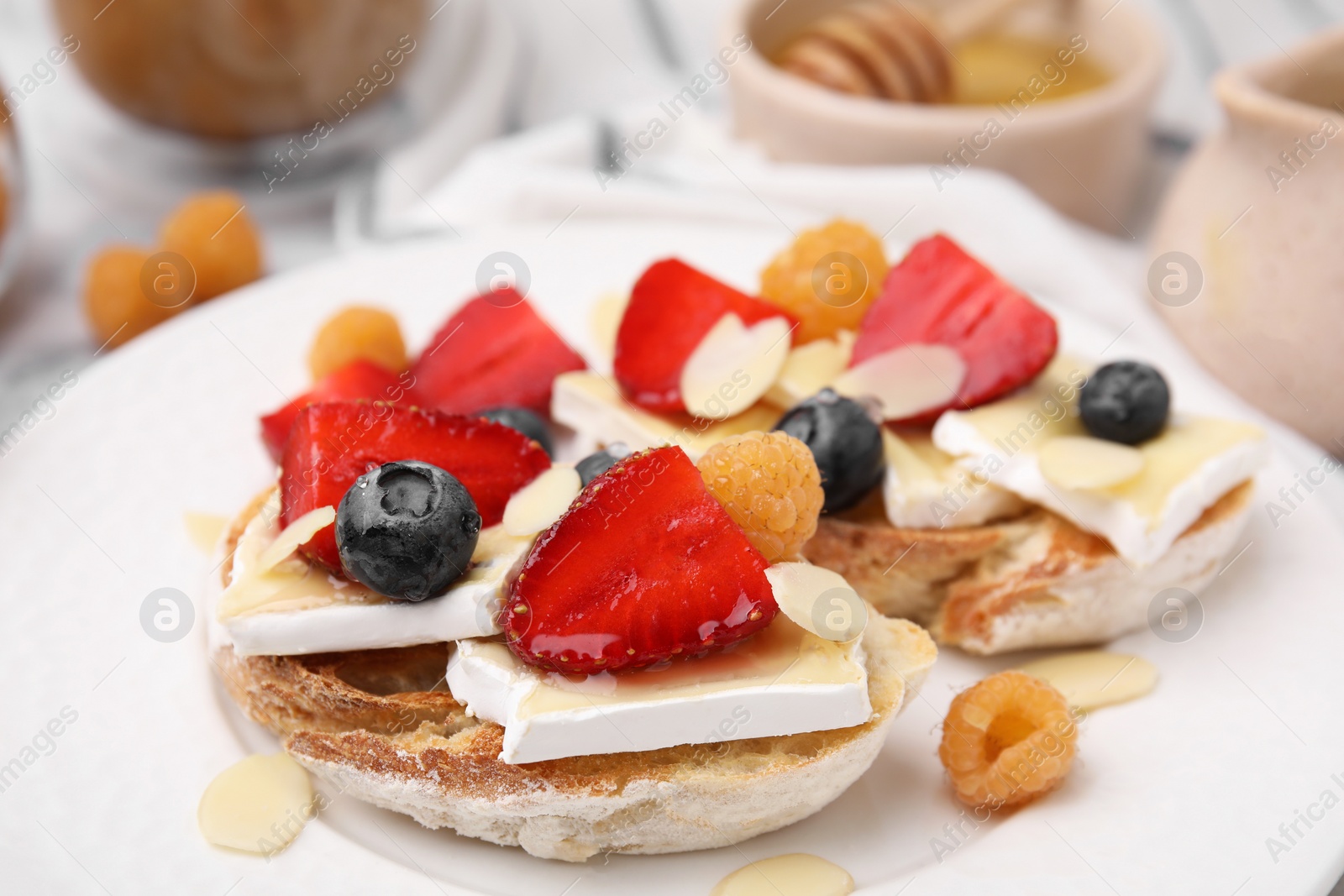 Photo of Tasty sandwiches with brie cheese, fresh berries and almond flakes on white plate, closeup