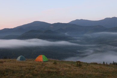 Photo of Picturesque view of mountain landscape with fog and camping tents in early morning
