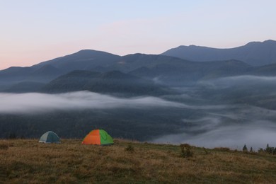 Picturesque view of mountain landscape with fog and camping tents in early morning