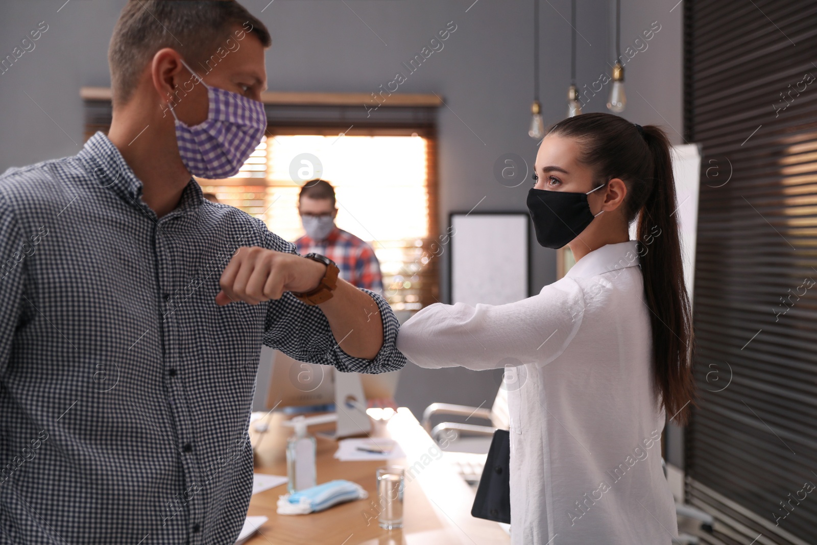 Photo of Coworkers with protective masks making elbow bump in office. Informal greeting during COVID-19 pandemic