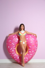 Beautiful young woman with inflatable heart near color wall
