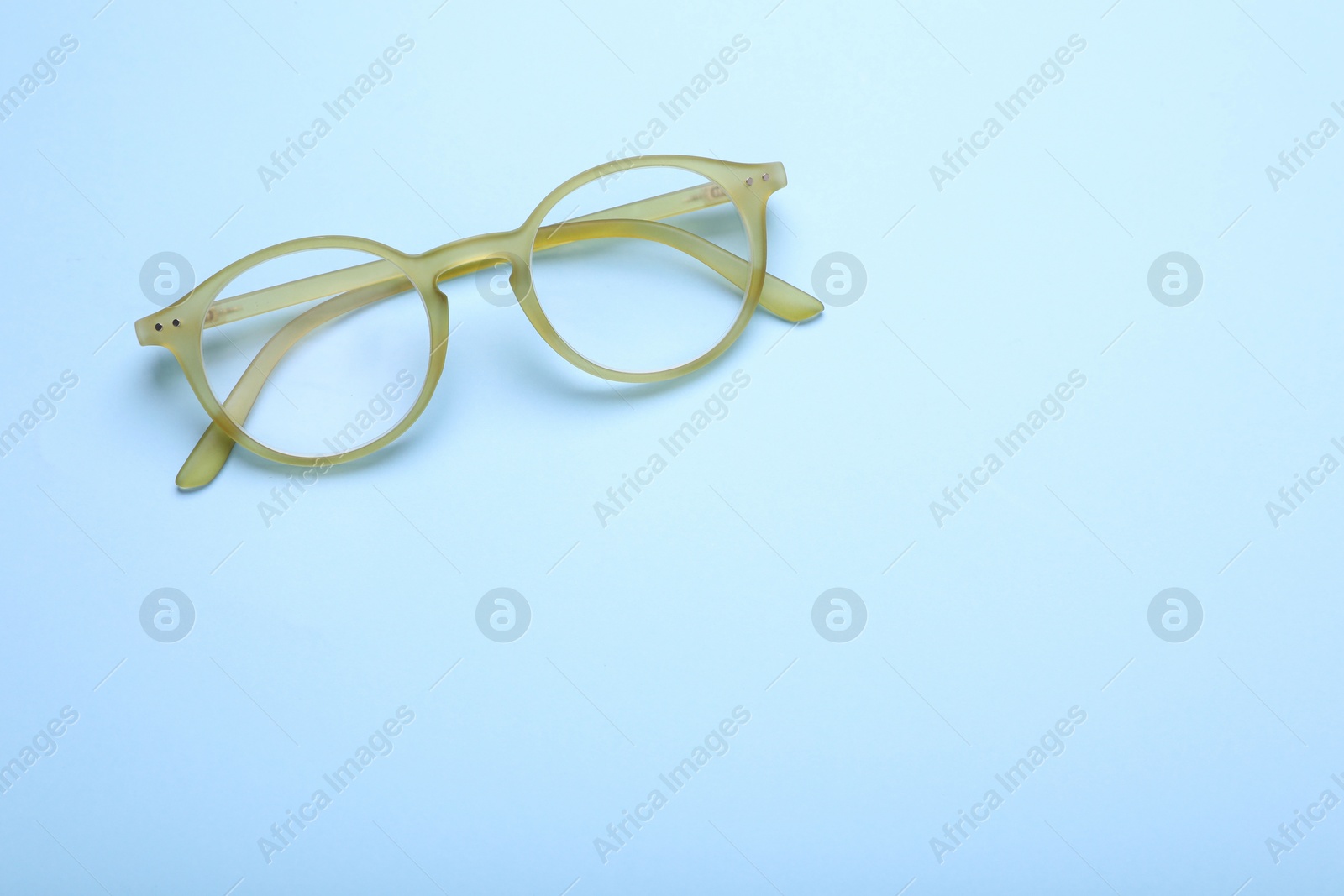 Photo of Glasses with corrective lenses on light blue background, top view. Space for text