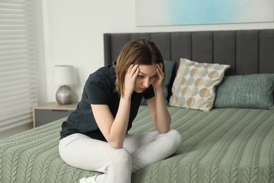 Photo of Sad young woman sitting on bed at home, space for text