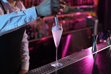 Photo of Bartender adding foam onto alcoholic cocktail at counter in bar, closeup