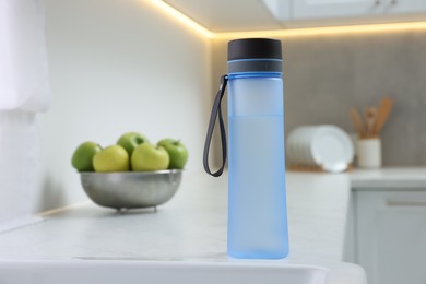 Stylish thermo bottle on white countertop in kitchen. Space for text