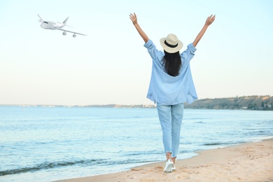Happy young woman on beach under sky with flying airplane. Summer vacation