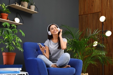 Happy woman listening to music in armchair at home. Indoor plants for trendy interior design