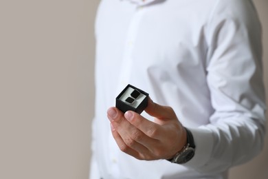 Photo of Stylish man holding box with cufflinks against beige background, closeup