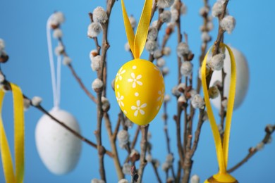 Photo of Beautiful willow branches with painted eggs on light blue background, closeup. Easter decor