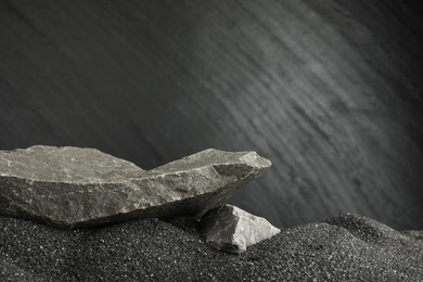 Photo of Presentation of product. Stone podium on black sand against dark textured background. Space for text