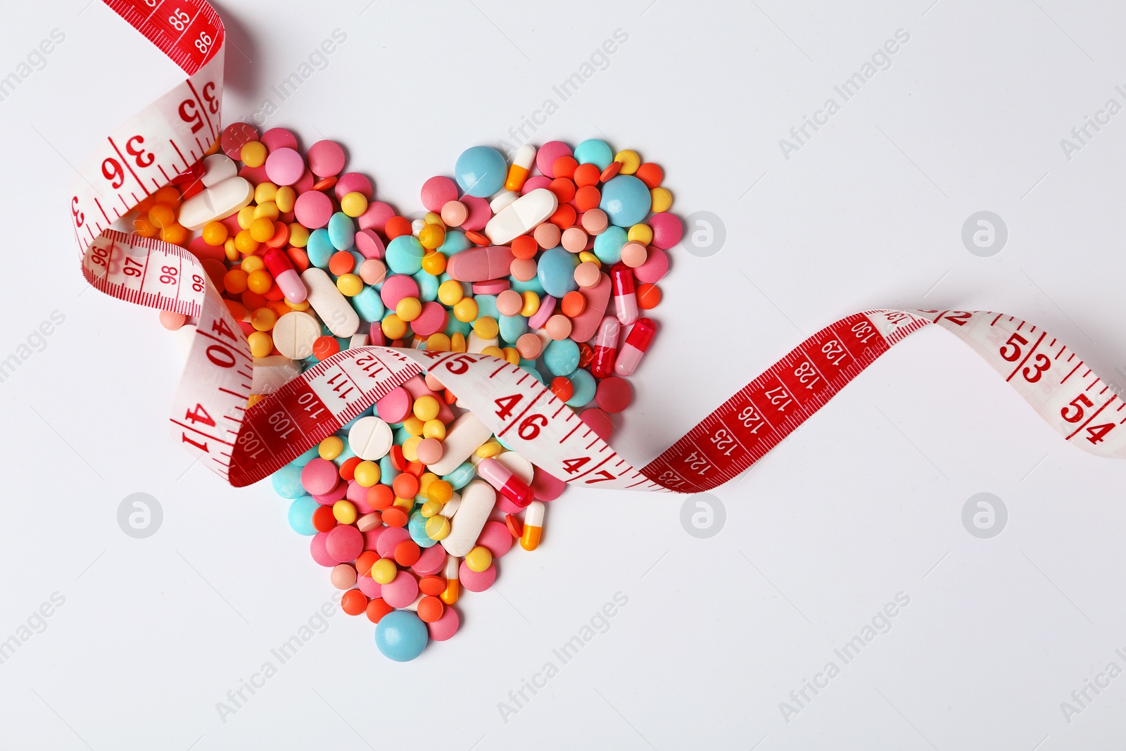 Photo of Heart shape made of Weight loss pills and measuring tape on white background, top view