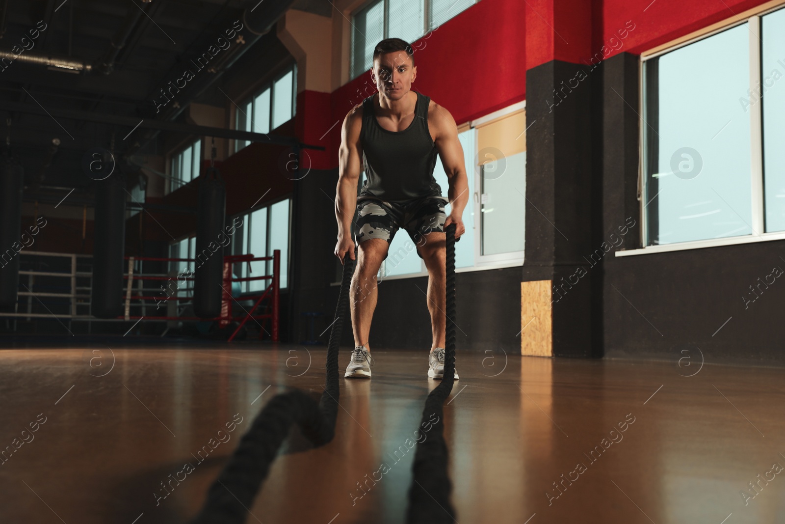 Photo of Man working out with battle ropes in modern gym