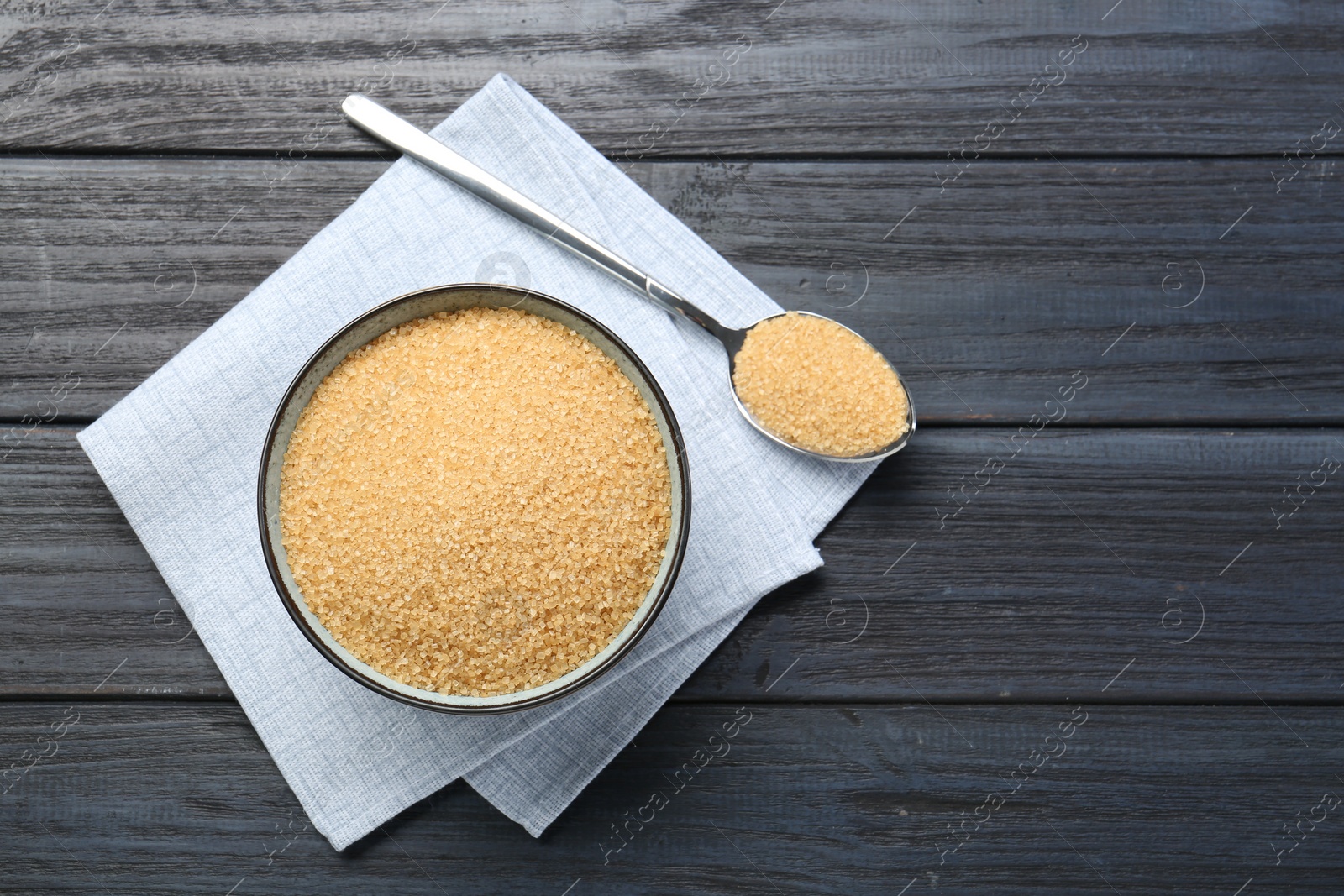 Photo of Brown sugar in bowl and spoon on black wooden table, flat lay. Space for text