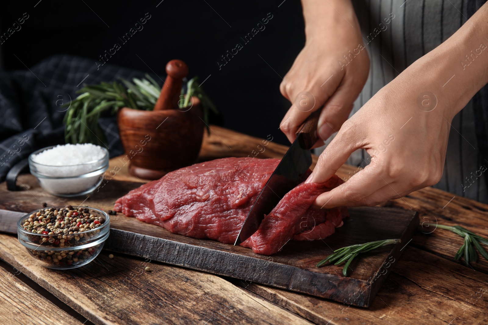 Photo of Woman cutting fresh raw meat at wooden table, closeup