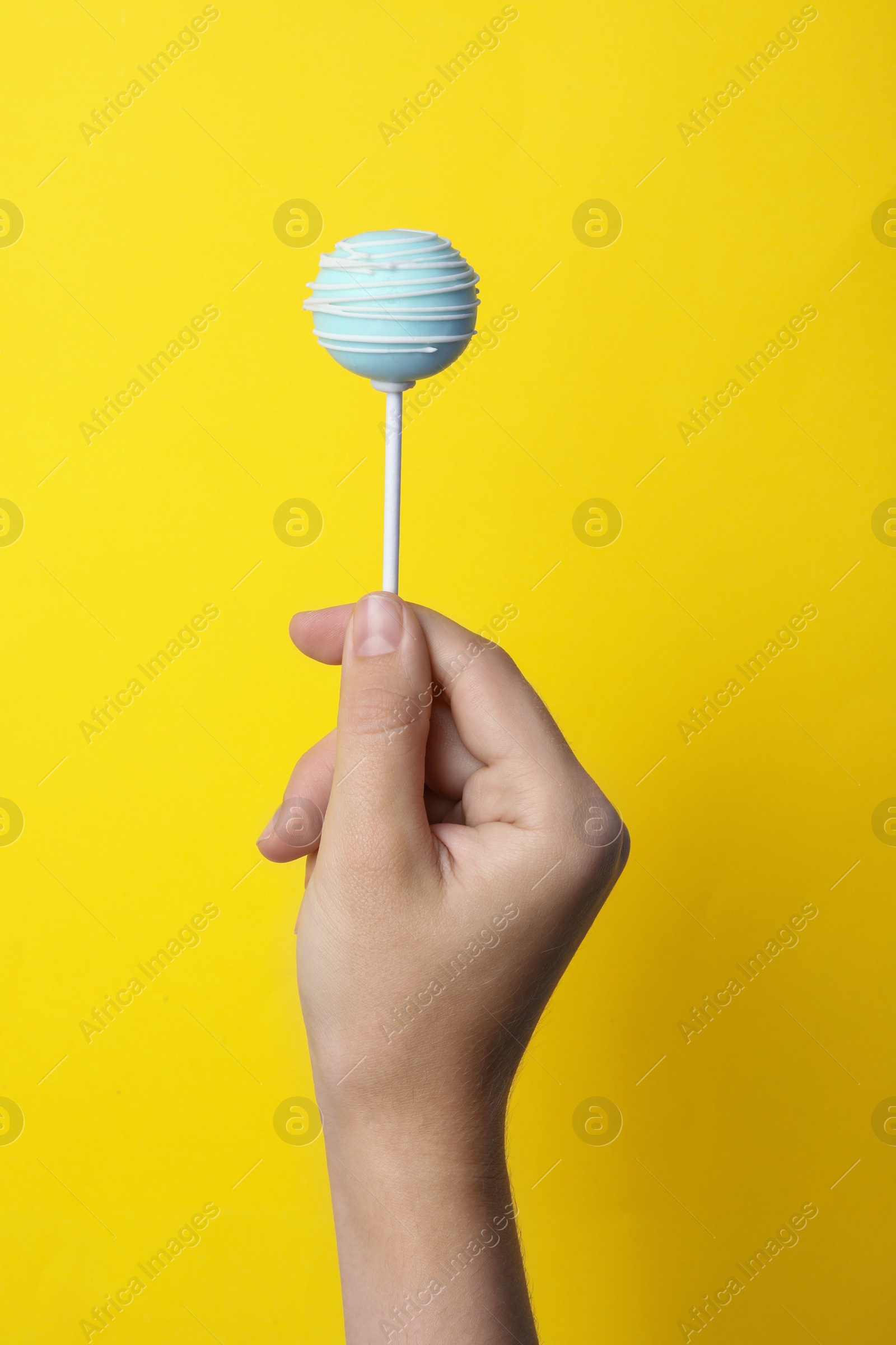 Photo of Woman holding sweet cake pop on yellow background, closeup