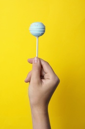 Photo of Woman holding sweet cake pop on yellow background, closeup