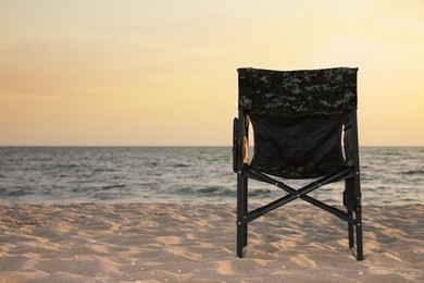 Camping chair on sandy beach near sea, space for text