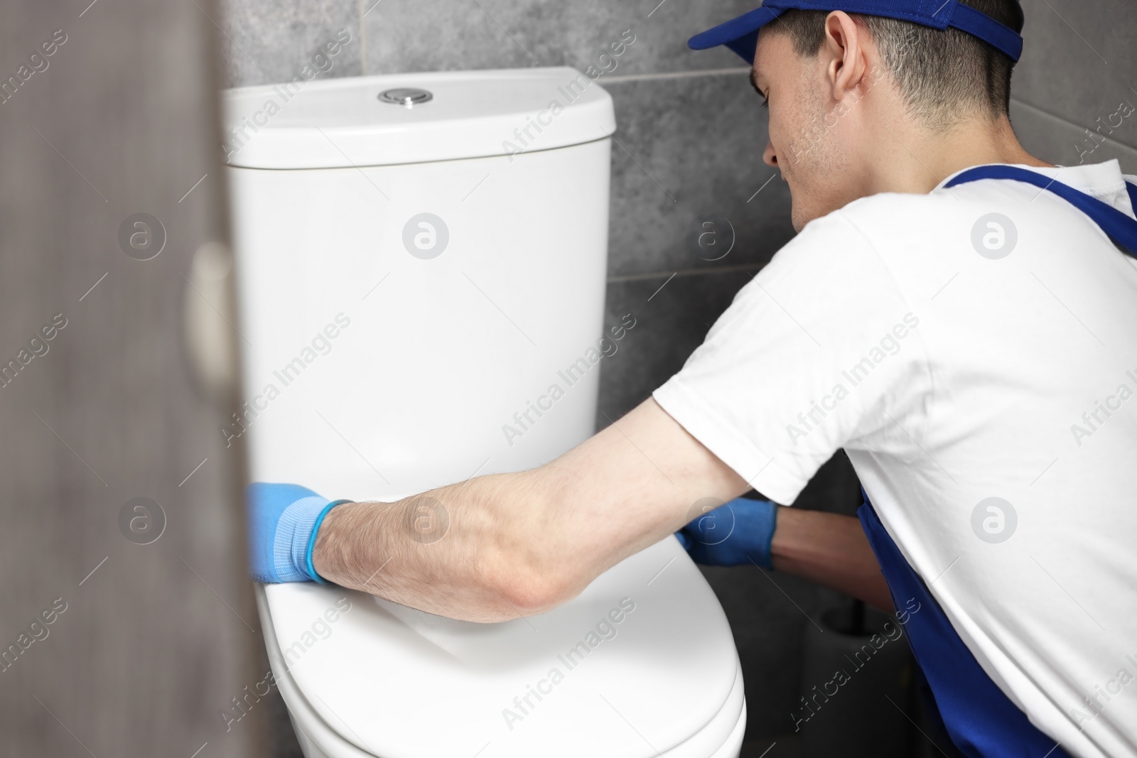Photo of Plumber wearing protective gloves repairing toilet bowl in water closet