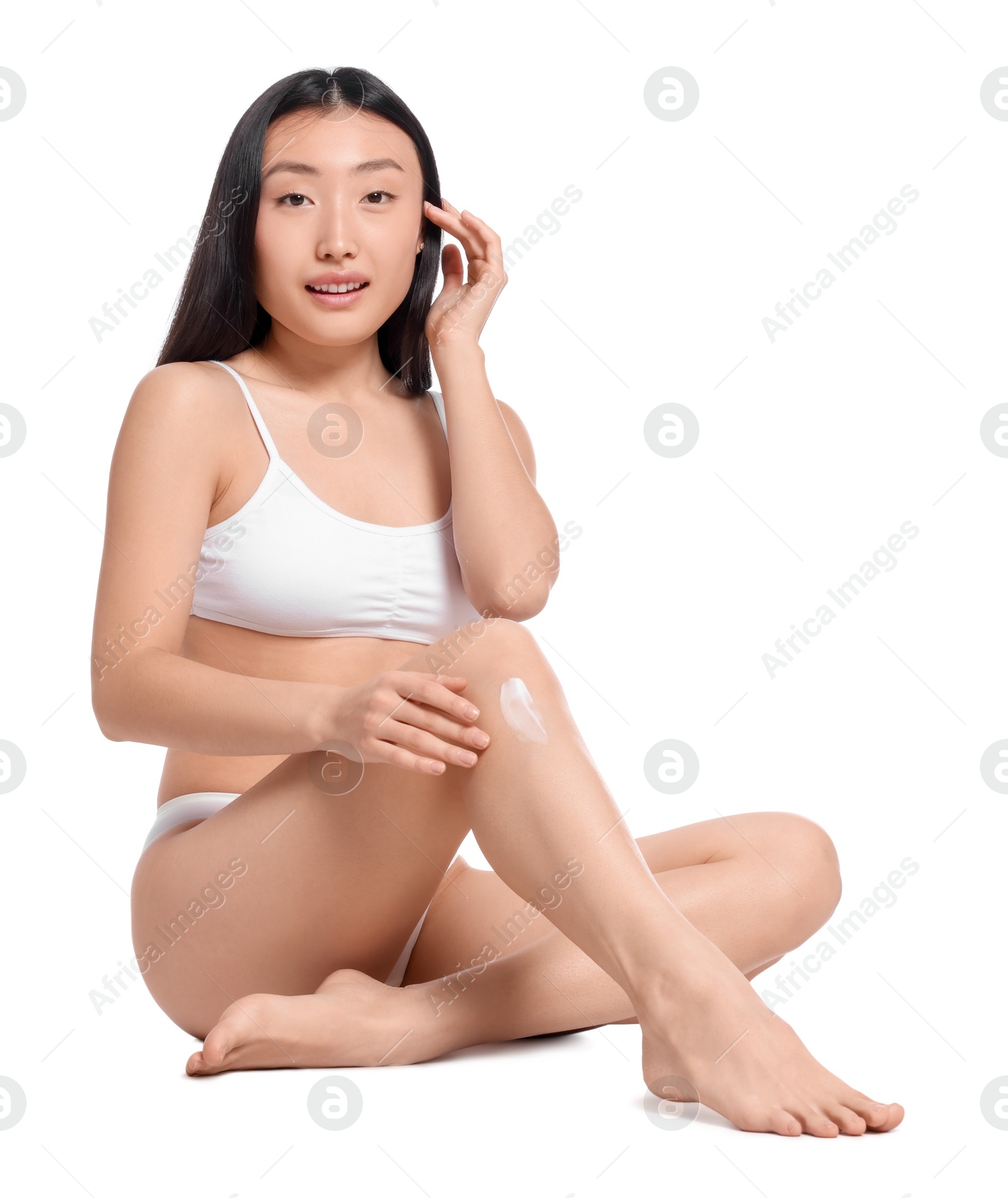 Photo of Beautiful young Asian woman applying body cream onto leg on white background