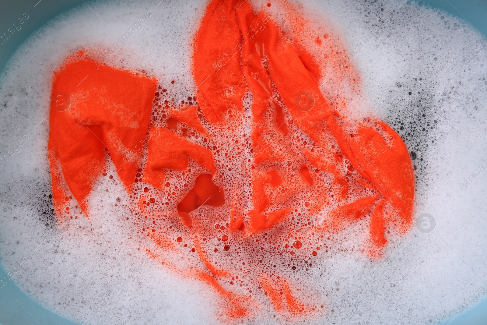 Photo of Orange garment in suds, top view. Hand washing laundry