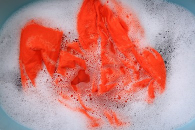 Photo of Orange garment in suds, top view. Hand washing laundry