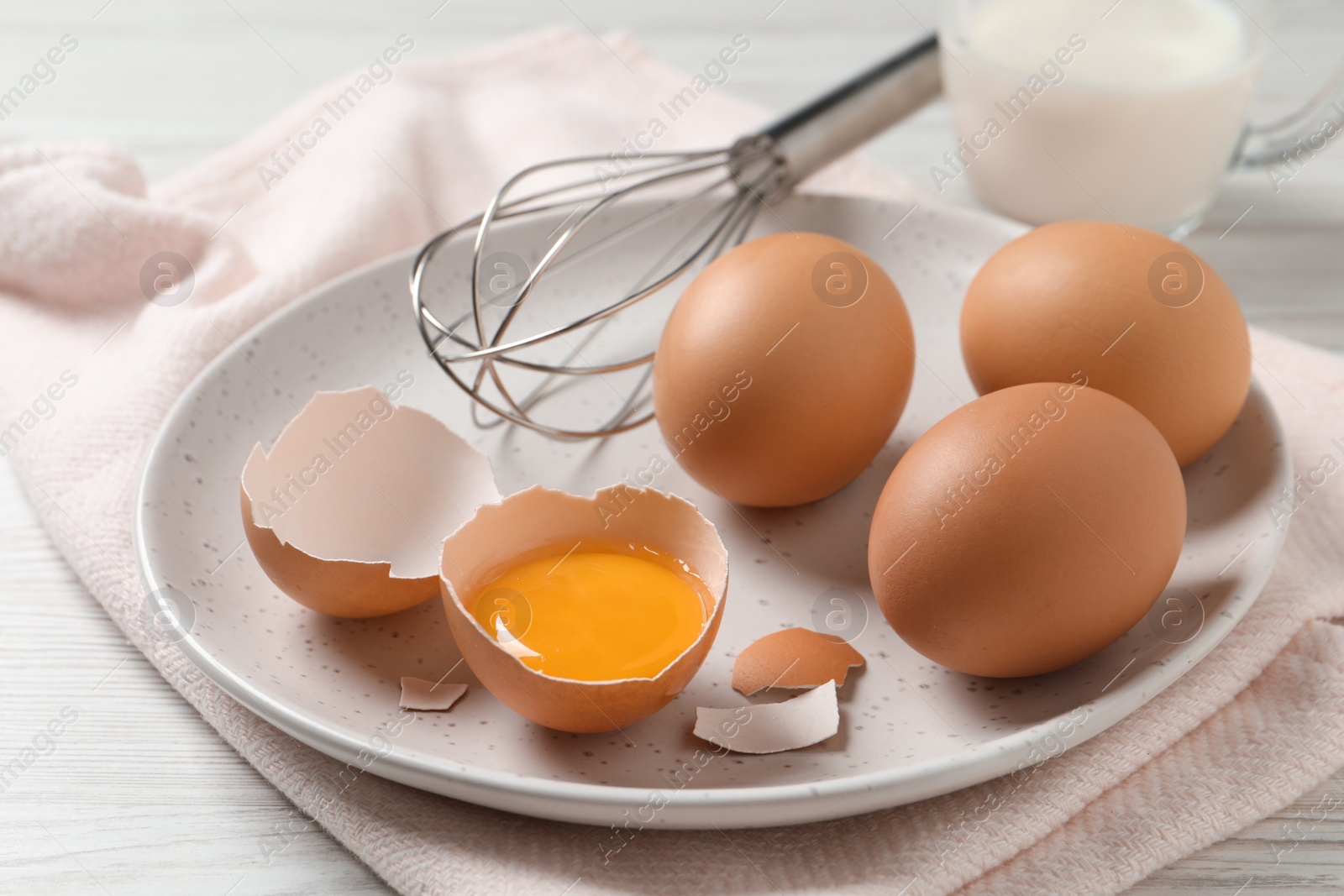 Photo of Chicken eggs and whisk on white wooden table, closeup