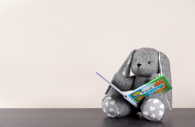 Adorable stuffed bunny with book on table against light background, space for text. Child room elements