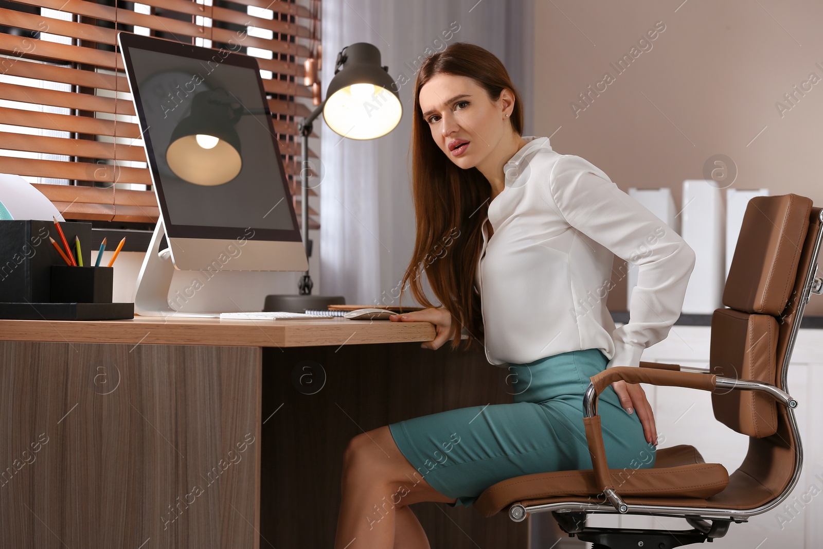 Photo of Young woman suffering from hemorrhoid at workplace in office