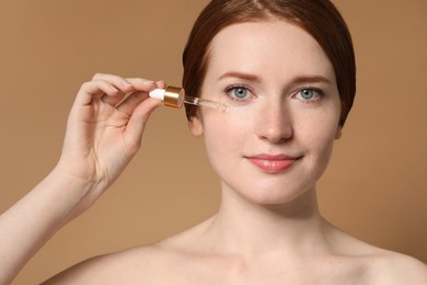 Photo of Beautiful woman with freckles applying cosmetic serum onto her face on beige background