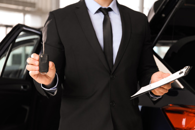 Photo of Salesman with key and clipboard near car in dealership, closeup
