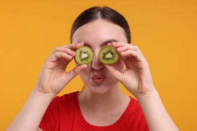 Photo of Woman covering eyes with halves of kiwi on orange background