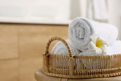 Photo of Rolled towels on wicker table in bathroom, closeup. Space for text
