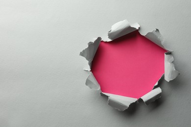 Hole in white paper on pink background, space for text