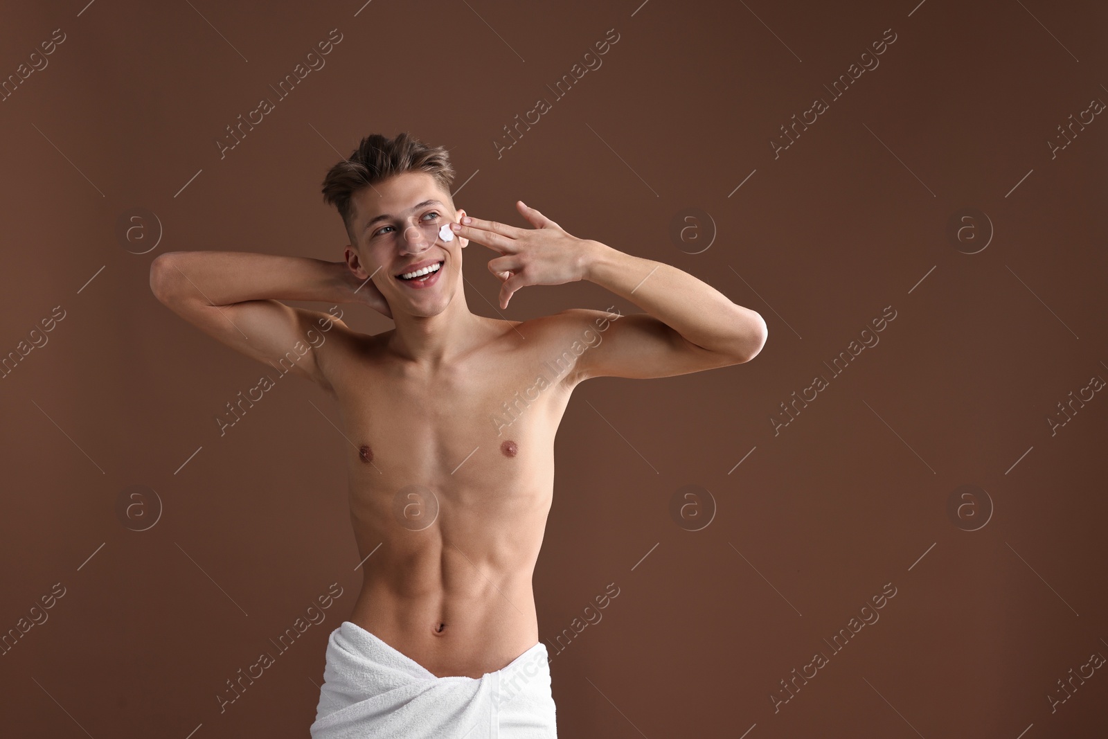 Photo of Handsome man applying moisturizing cream onto his face on brown background. Space for text