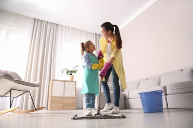 Mother and daughter mopping floor in living room at home